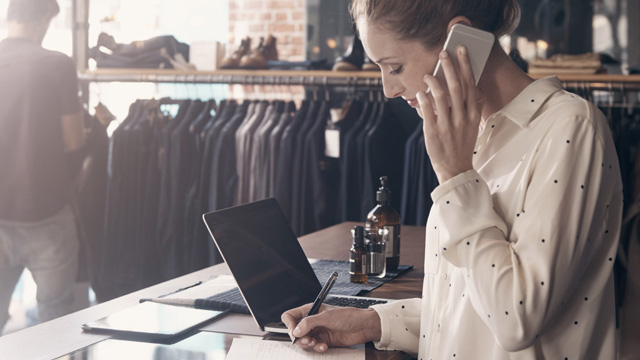 Clothing shop woman working in mobile with laptop